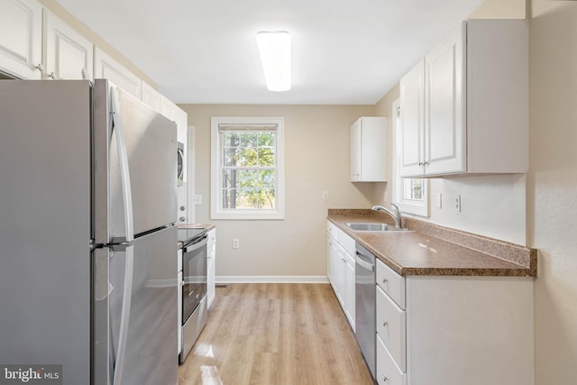 kitchen with sink, appliances with stainless steel finishes, light hardwood / wood-style flooring, and white cabinetry