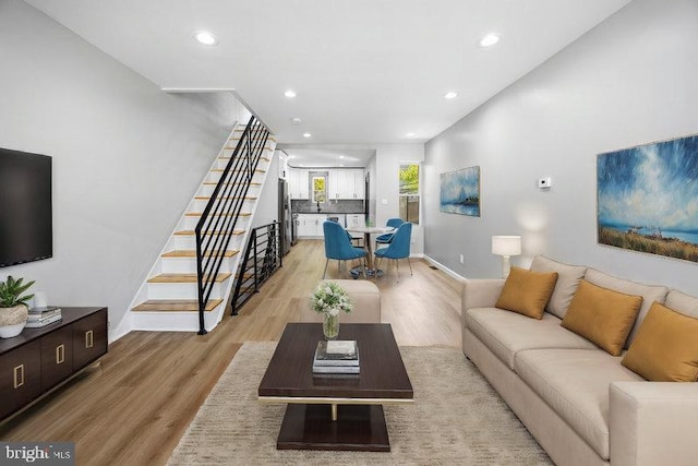 living room featuring light wood finished floors, baseboards, recessed lighting, and stairway