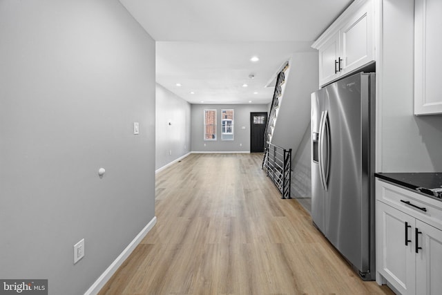 kitchen featuring dark stone countertops, stainless steel fridge, white cabinets, and light wood-type flooring