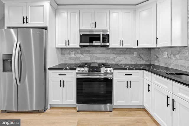 kitchen with white cabinets, stainless steel appliances, dark stone countertops, backsplash, and light wood-style floors
