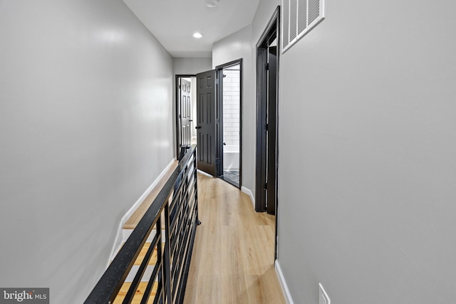 hallway featuring light wood finished floors, baseboards, visible vents, recessed lighting, and an upstairs landing
