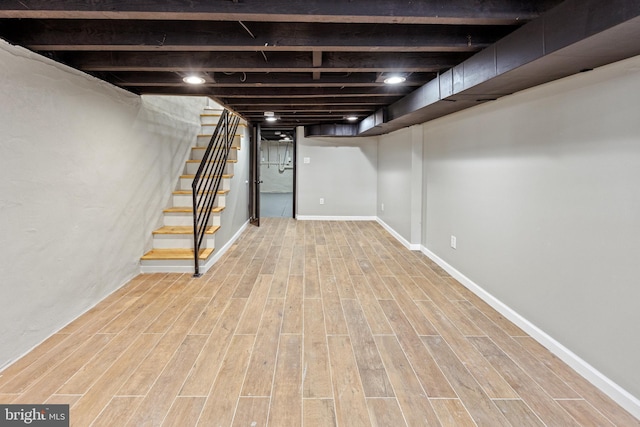 finished basement featuring baseboards, light wood-style floors, and stairway
