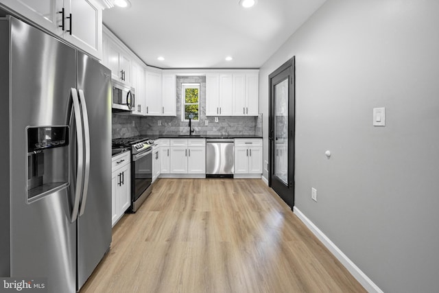 kitchen with light wood finished floors, a sink, dark countertops, backsplash, and appliances with stainless steel finishes
