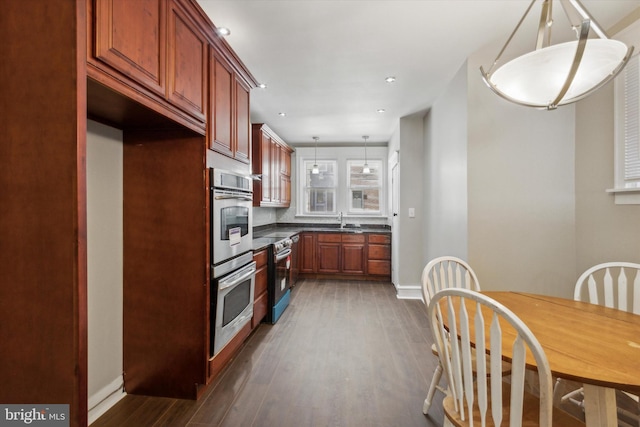 kitchen featuring appliances with stainless steel finishes, sink, backsplash, hanging light fixtures, and dark wood-type flooring