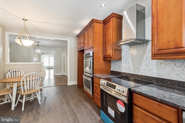 kitchen featuring dark stone counters, dark hardwood / wood-style floors, pendant lighting, wall chimney exhaust hood, and stainless steel appliances