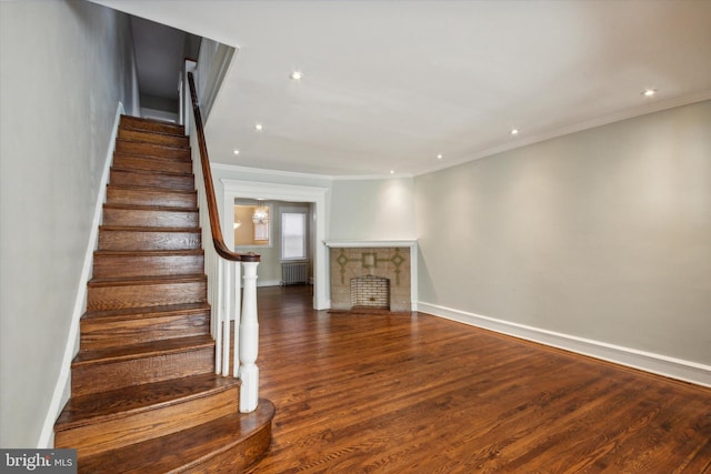 stairway featuring crown molding, hardwood / wood-style flooring, radiator heating unit, and a fireplace