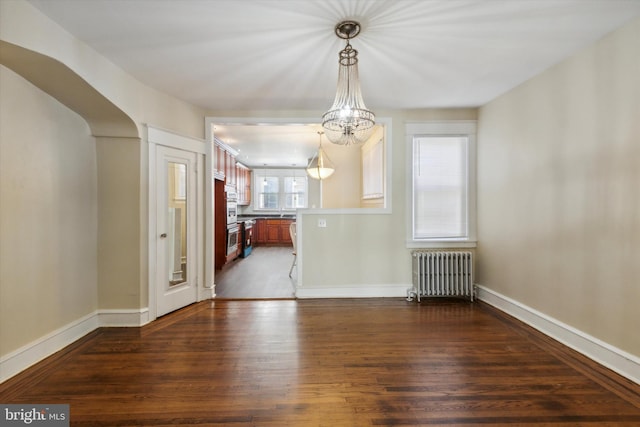 unfurnished dining area with an inviting chandelier, dark hardwood / wood-style floors, a healthy amount of sunlight, and radiator