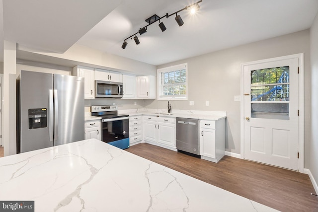 kitchen with rail lighting, stainless steel appliances, light stone counters, and white cabinets