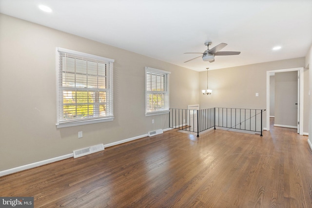 empty room featuring ceiling fan with notable chandelier and dark hardwood / wood-style floors