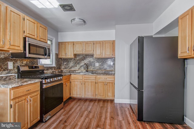 kitchen with light brown cabinets, decorative backsplash, appliances with stainless steel finishes, light wood-type flooring, and sink