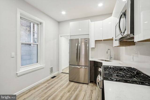 kitchen featuring white cabinets, light wood-type flooring, appliances with stainless steel finishes, and sink