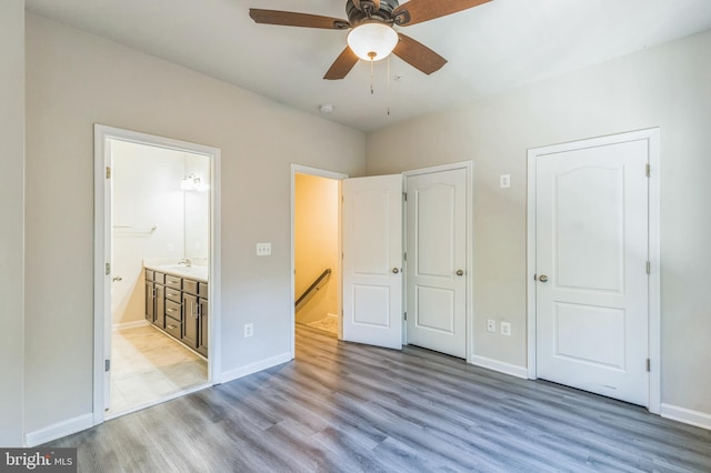 unfurnished bedroom featuring sink, multiple closets, light hardwood / wood-style floors, ceiling fan, and connected bathroom