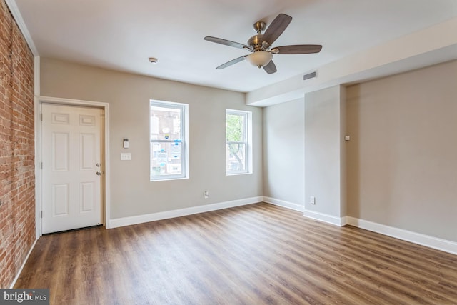 spare room with dark hardwood / wood-style floors, brick wall, and ceiling fan