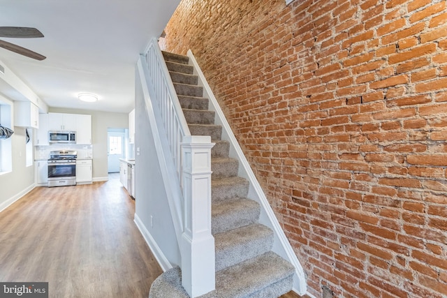 staircase with brick wall and hardwood / wood-style flooring