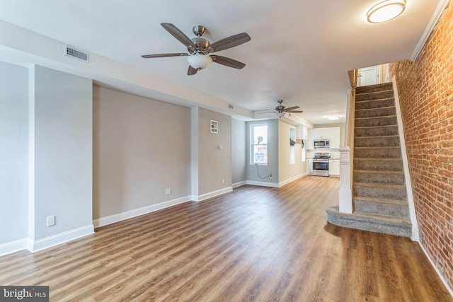 unfurnished living room featuring wood-type flooring, brick wall, and ceiling fan