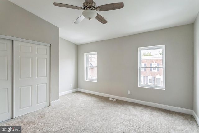 unfurnished bedroom featuring multiple windows, a closet, light colored carpet, and ceiling fan