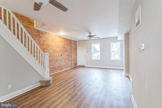 unfurnished living room with hardwood / wood-style flooring, brick wall, and ceiling fan