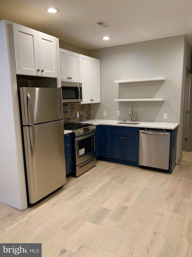 kitchen featuring stainless steel appliances, sink, light wood-type flooring, blue cabinets, and white cabinets