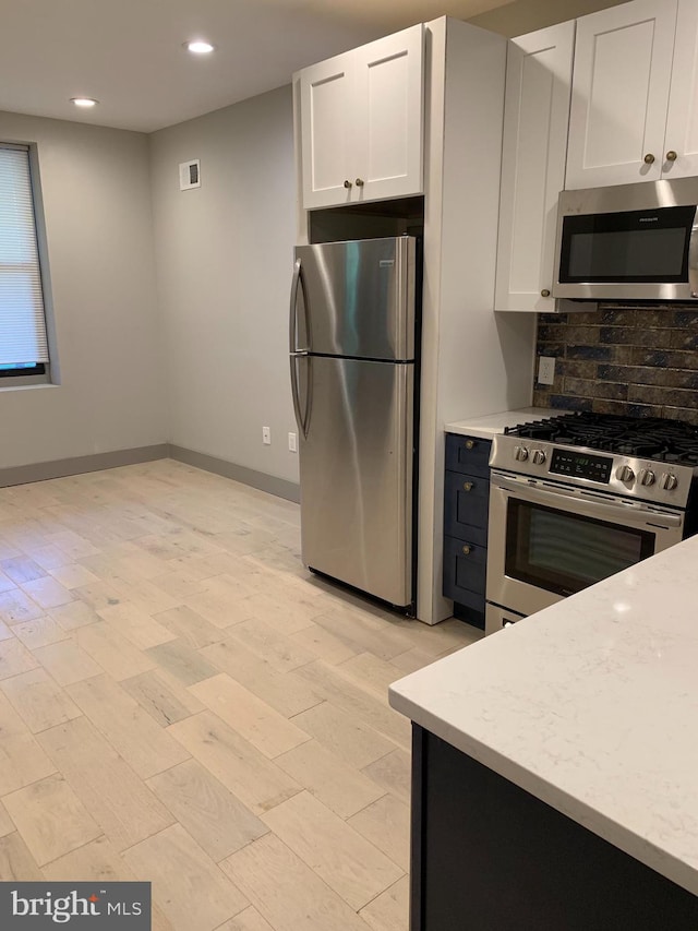 kitchen featuring backsplash, white cabinetry, light stone countertops, light wood-type flooring, and stainless steel appliances