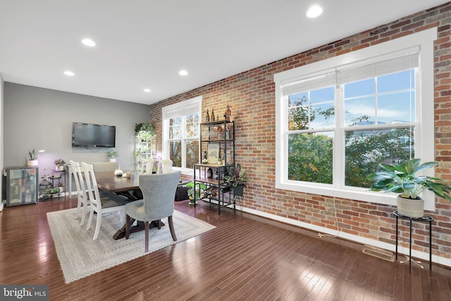 dining area with dark hardwood / wood-style flooring and brick wall