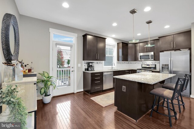 kitchen with stainless steel appliances, dark brown cabinetry, dark hardwood / wood-style floors, hanging light fixtures, and sink