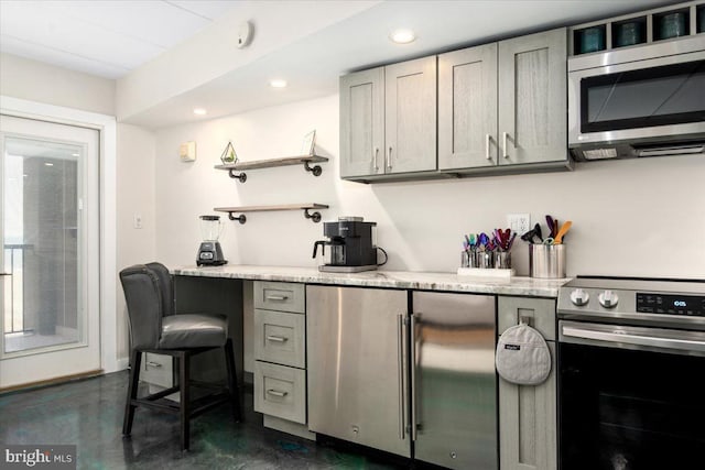 kitchen featuring gray cabinets, a kitchen breakfast bar, light stone countertops, and stainless steel appliances