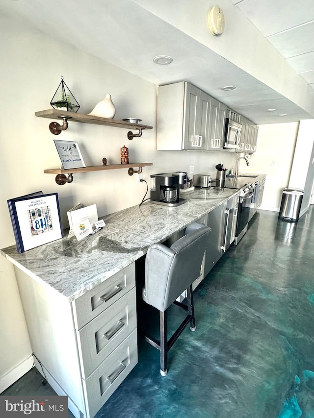 kitchen with sink, a kitchen bar, stainless steel appliances, gray cabinets, and light stone counters