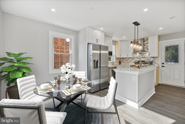 kitchen with light hardwood / wood-style floors, white cabinetry, appliances with stainless steel finishes, wall chimney exhaust hood, and pendant lighting