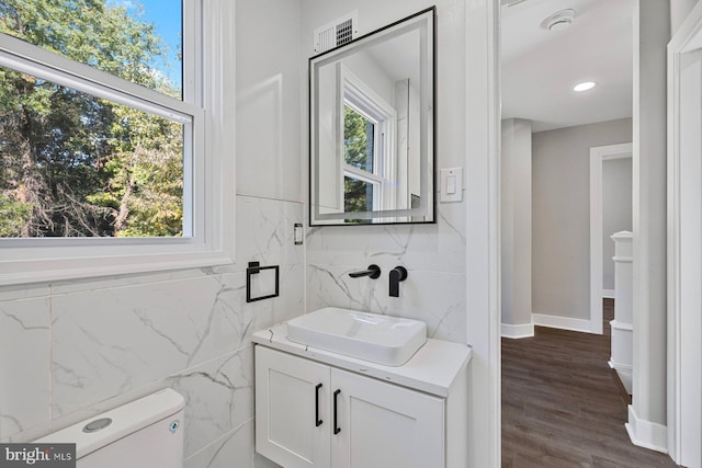 half bath with vanity, toilet, tile walls, baseboards, and wood finished floors