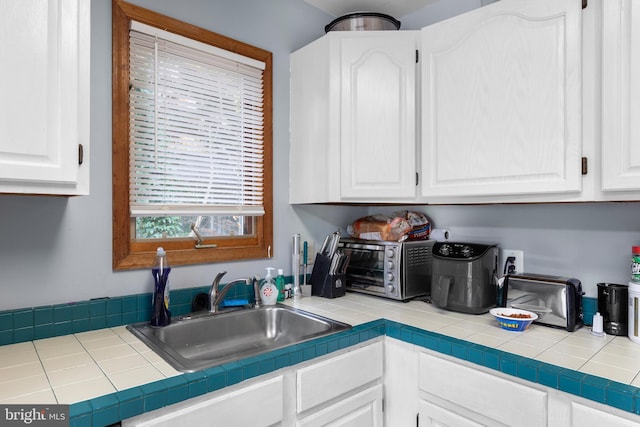 kitchen with tile countertops, sink, and white cabinets