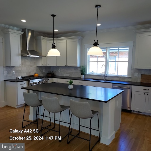 kitchen featuring wall chimney range hood, dark wood-type flooring, sink, stainless steel dishwasher, and white cabinets