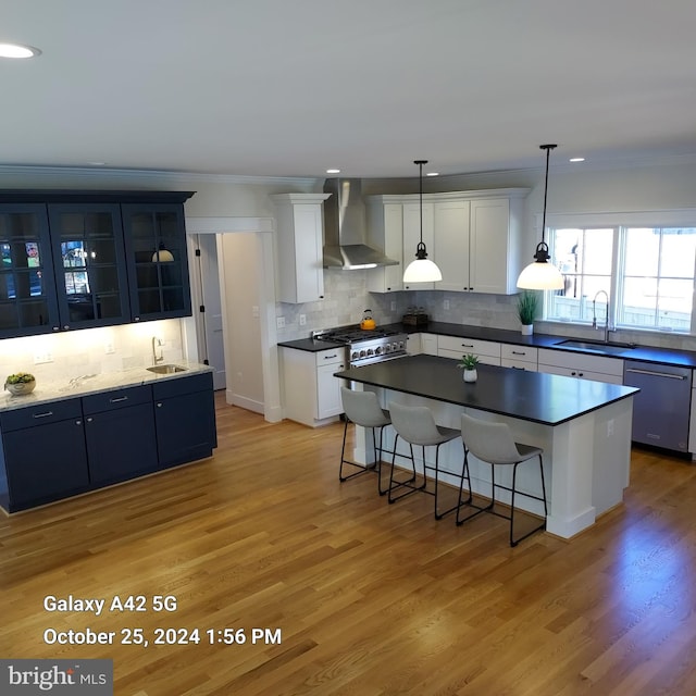 kitchen with wall chimney exhaust hood, sink, a center island, white cabinets, and appliances with stainless steel finishes