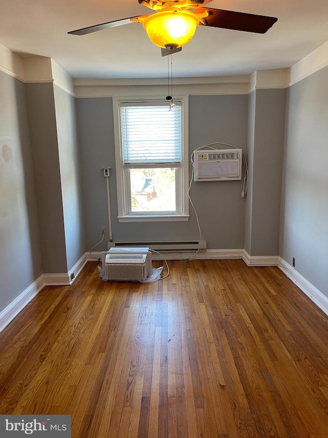 empty room featuring a wall unit AC, baseboard heating, wood-type flooring, and ornamental molding