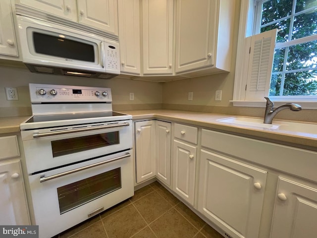 kitchen with dark tile patterned floors, sink, white cabinets, and white appliances