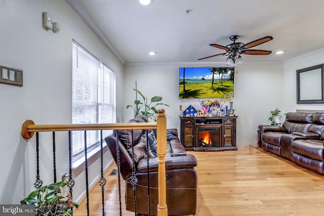 living room with light hardwood / wood-style floors, ceiling fan, and ornamental molding