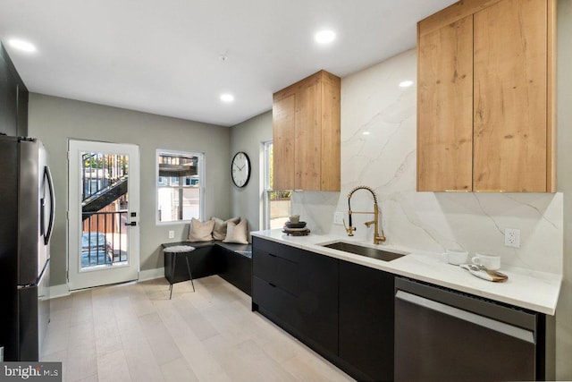 kitchen with sink, appliances with stainless steel finishes, decorative backsplash, and light hardwood / wood-style flooring