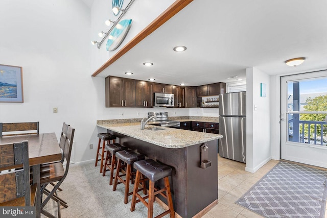 kitchen with appliances with stainless steel finishes, a kitchen bar, kitchen peninsula, dark brown cabinetry, and light tile patterned floors