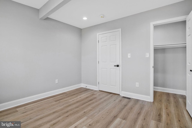 unfurnished bedroom with beam ceiling and light wood-type flooring