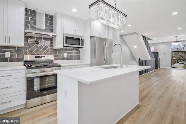 kitchen with white cabinets, an island with sink, wall chimney range hood, and appliances with stainless steel finishes