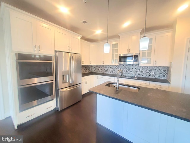 kitchen with dark stone counters, stainless steel appliances, sink, pendant lighting, and white cabinetry