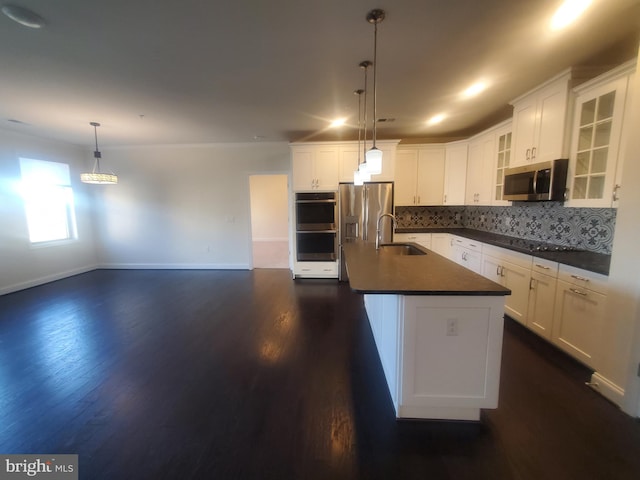 kitchen with stainless steel appliances, a kitchen island with sink, sink, decorative light fixtures, and white cabinetry