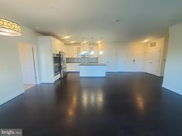 kitchen featuring backsplash, hanging light fixtures, a kitchen island, white cabinetry, and stainless steel refrigerator