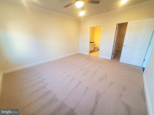 unfurnished bedroom featuring ceiling fan, ensuite bathroom, crown molding, light colored carpet, and a walk in closet