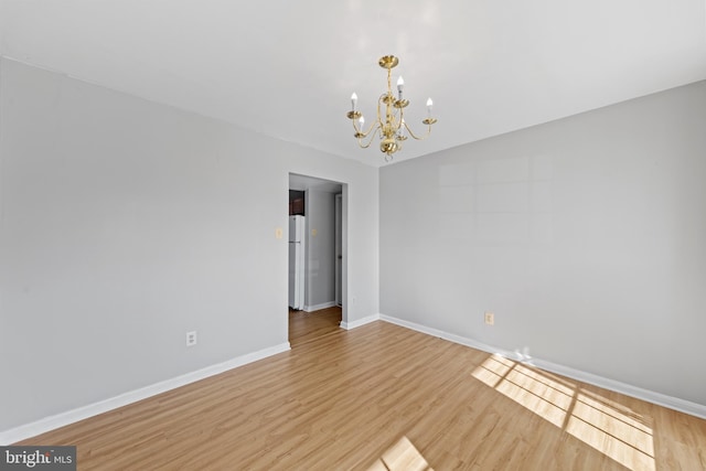 spare room featuring light wood-type flooring and a chandelier