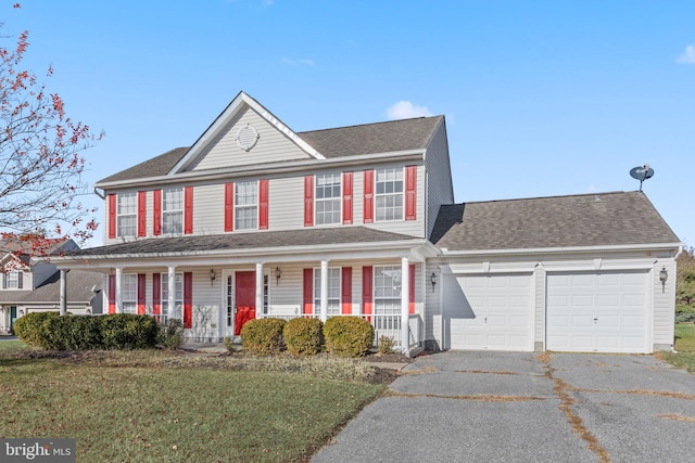 colonial home with a porch, a front yard, and a garage