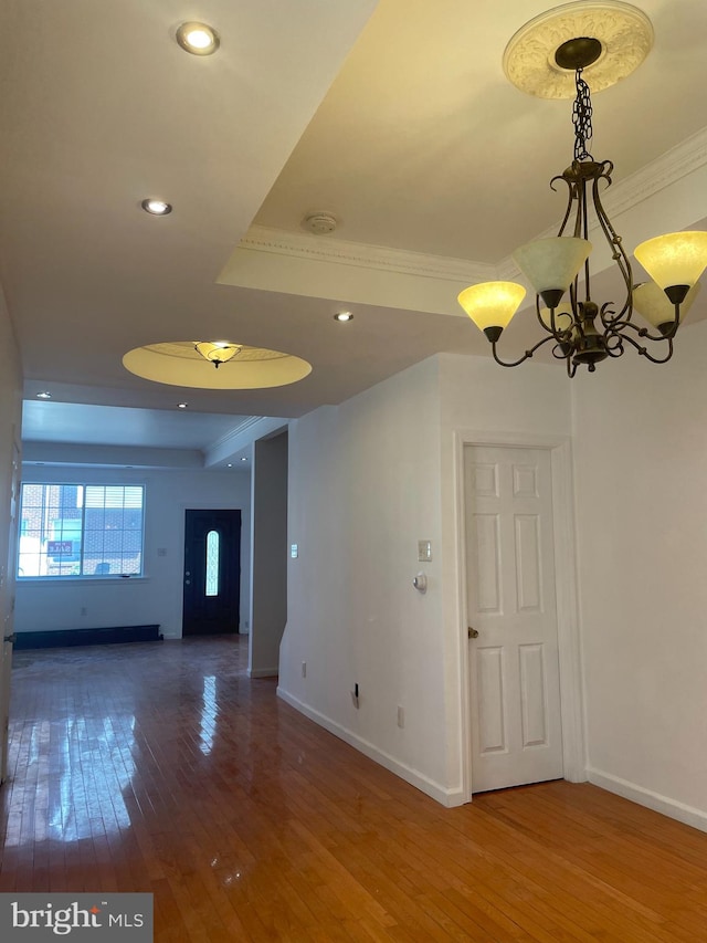 spare room featuring crown molding, wood-type flooring, a chandelier, and a raised ceiling