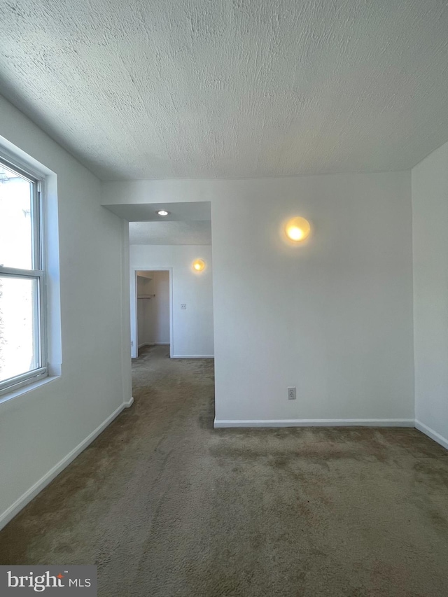 unfurnished room featuring a textured ceiling and dark colored carpet