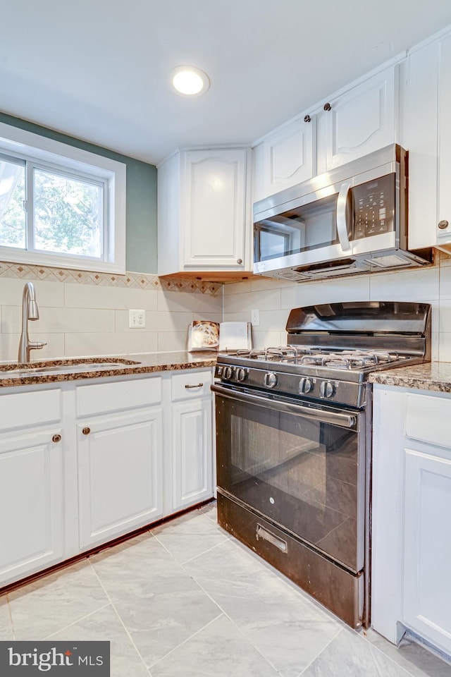 kitchen featuring stone counters, sink, black gas stove, white cabinetry, and decorative backsplash