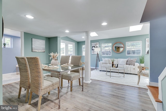 dining space with a healthy amount of sunlight, decorative columns, lofted ceiling, and light wood-type flooring