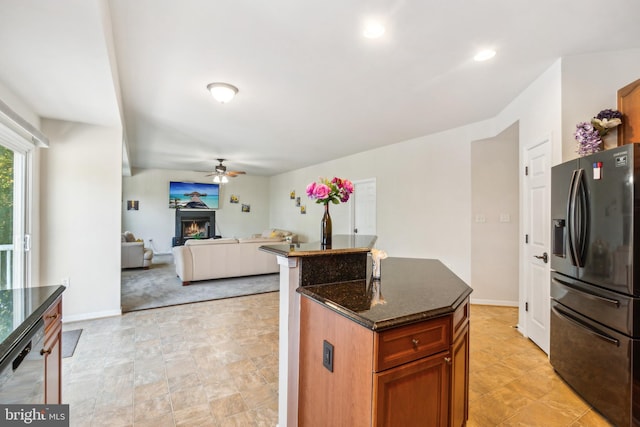 kitchen with a center island, dark stone counters, black refrigerator with ice dispenser, and ceiling fan